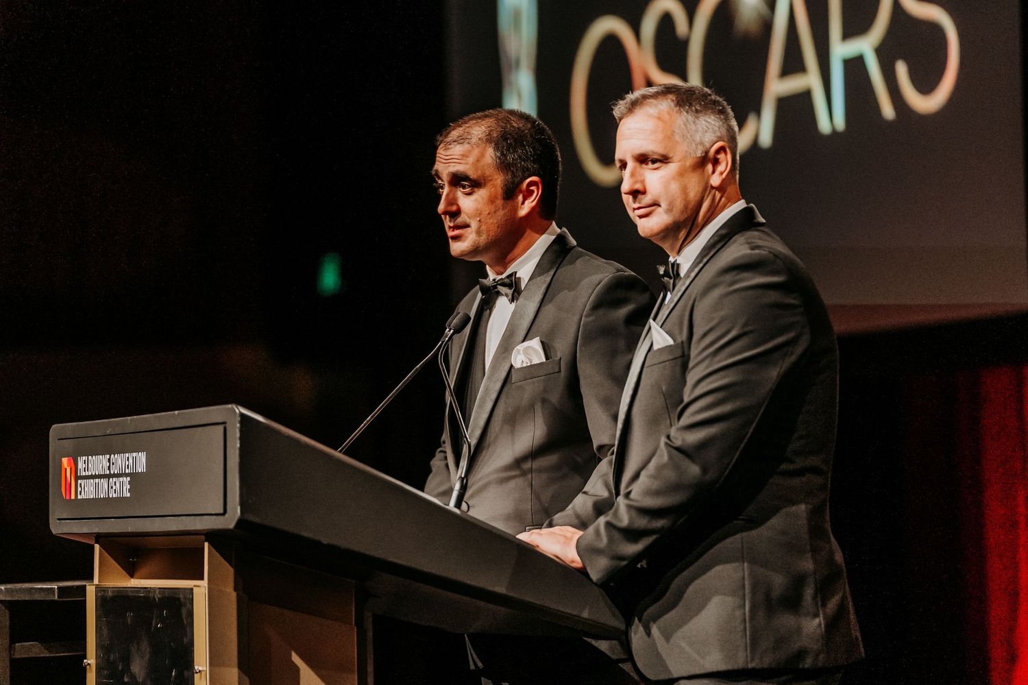 Two speakers stand at podiums on a stage during an awards ceremony presentation.
