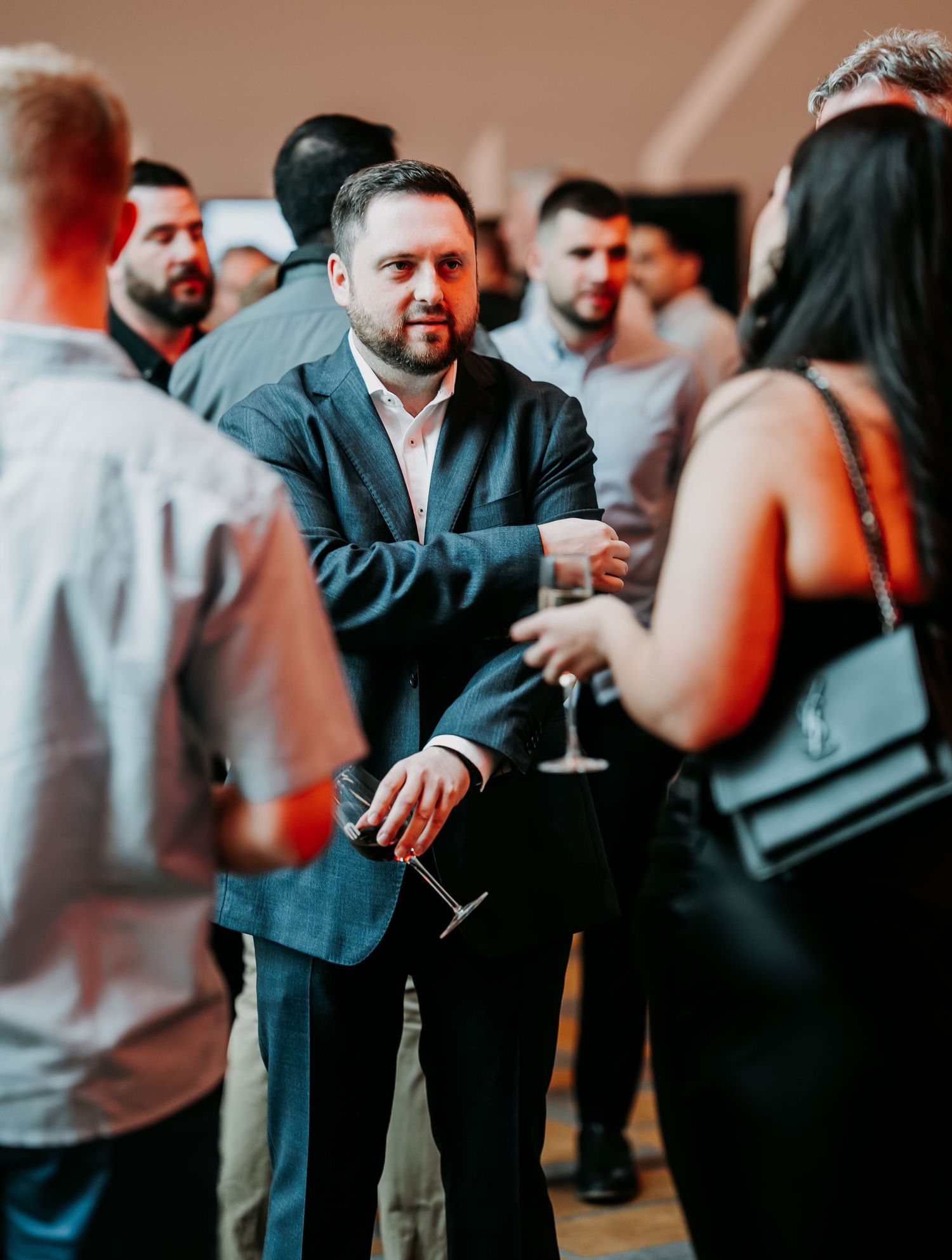 Group of people socializing at an elegant cocktail party with drinks in a dimly lit setting.