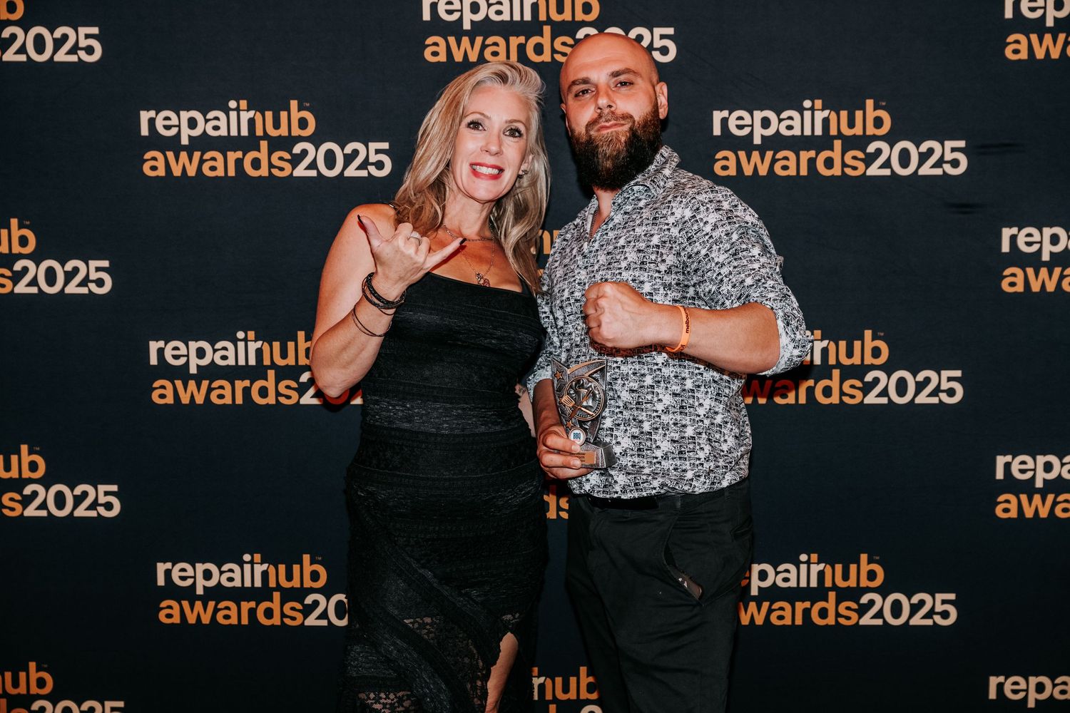 Two people in formal attire pose together at an awards show with glowing orange signage in the background.