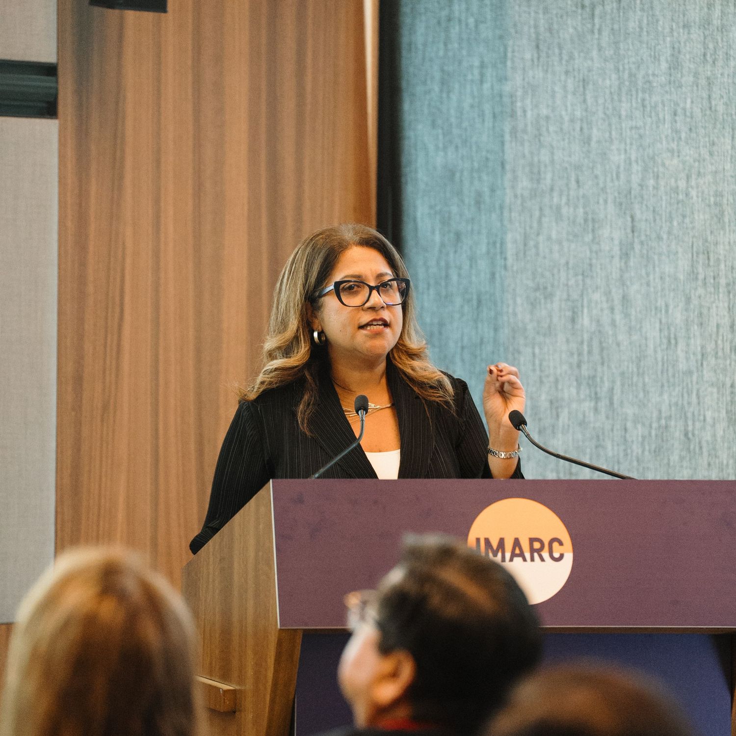 A speaker addresses an audience from behind a podium during a professional conference presentation.