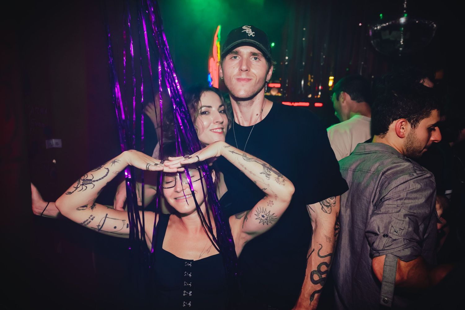 A group of people performing at a nightclub with colorful purple and green lighting in the background.