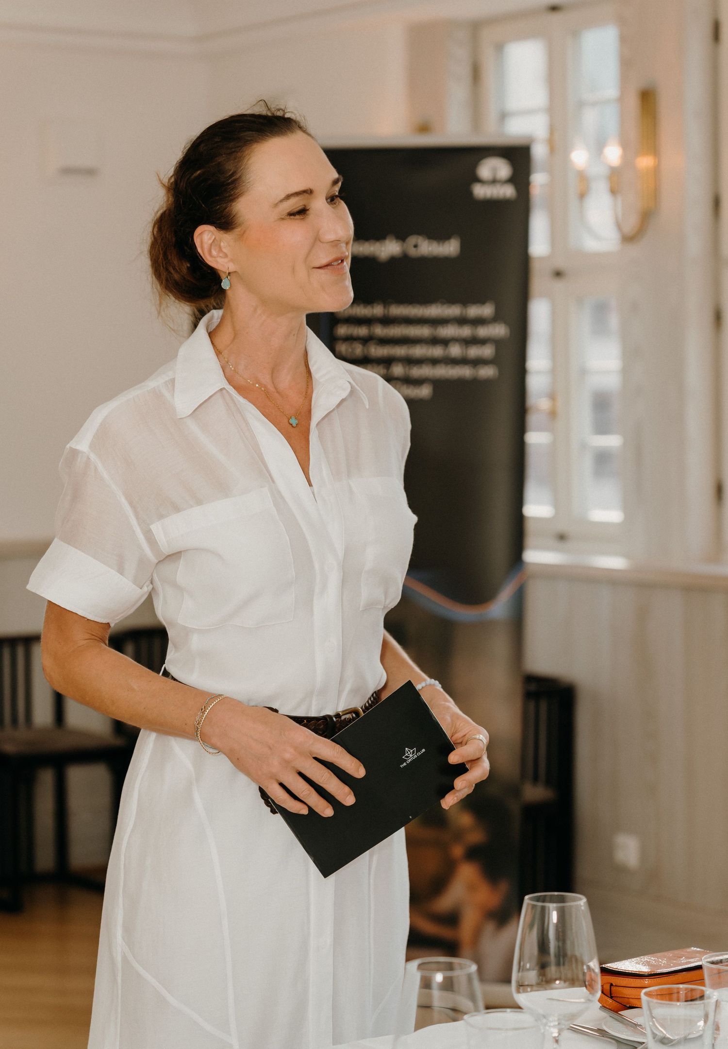 Woman in white shirt dress holds black folder at Google Cloud and Tata business event.