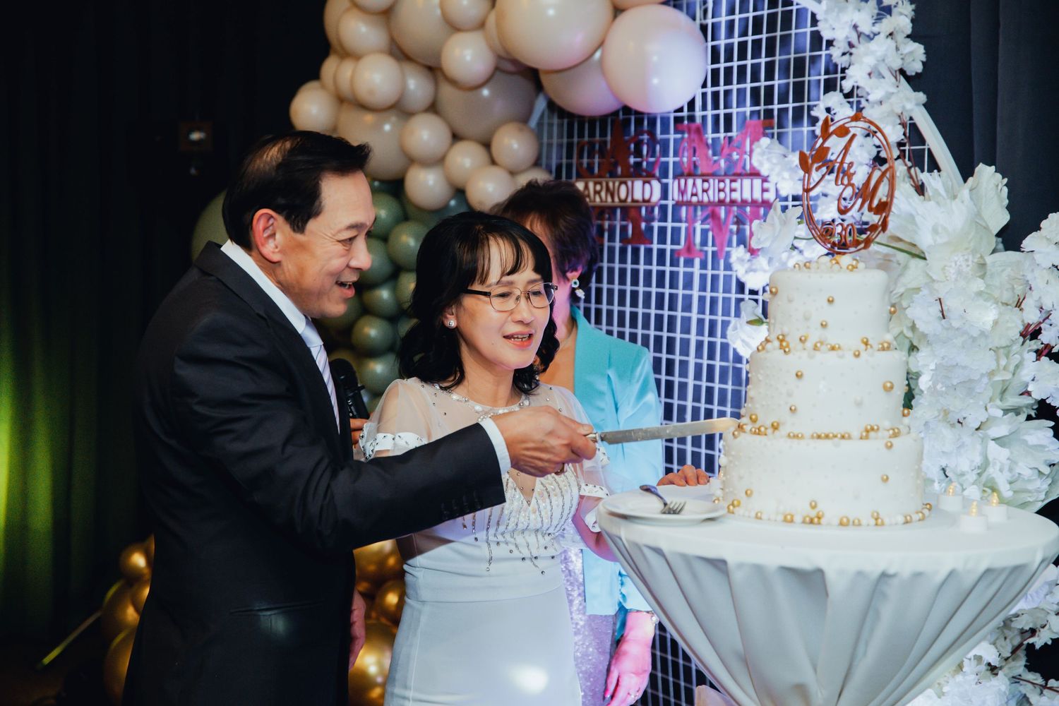 A pair shares a celebratory moment cutting their elegant white wedding cake at an indoor reception.