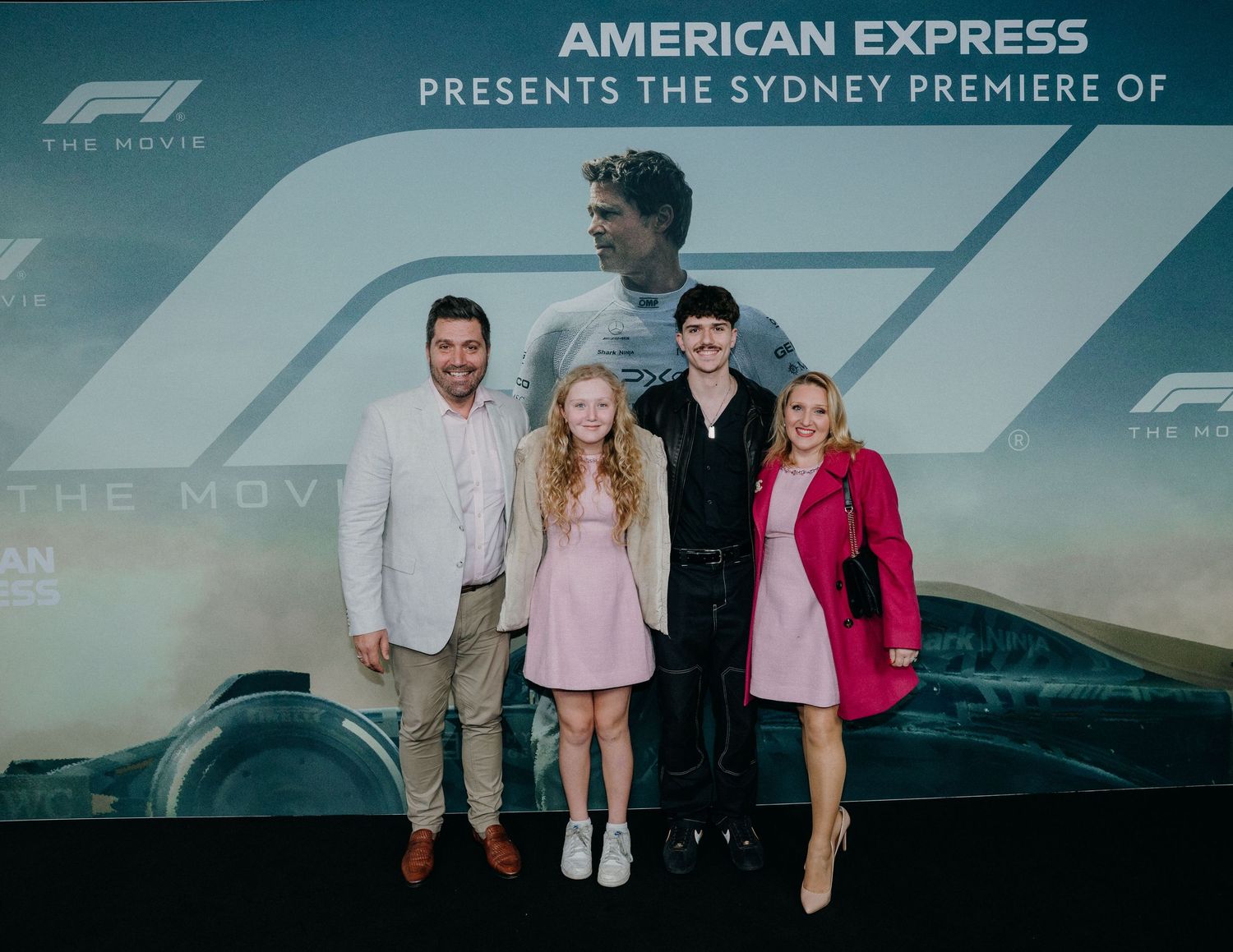 A group of four people pose at a Formula 1 movie premiere event with American Express branding in the background.