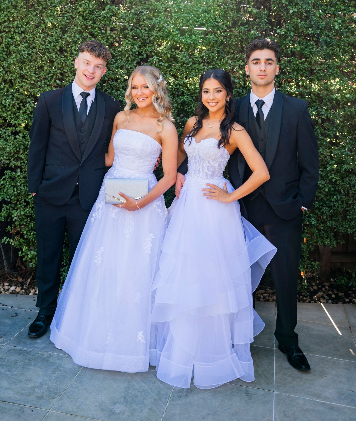 Little ones in elegant white dresses pose with adults in formal attire at an outdoor gathering.
