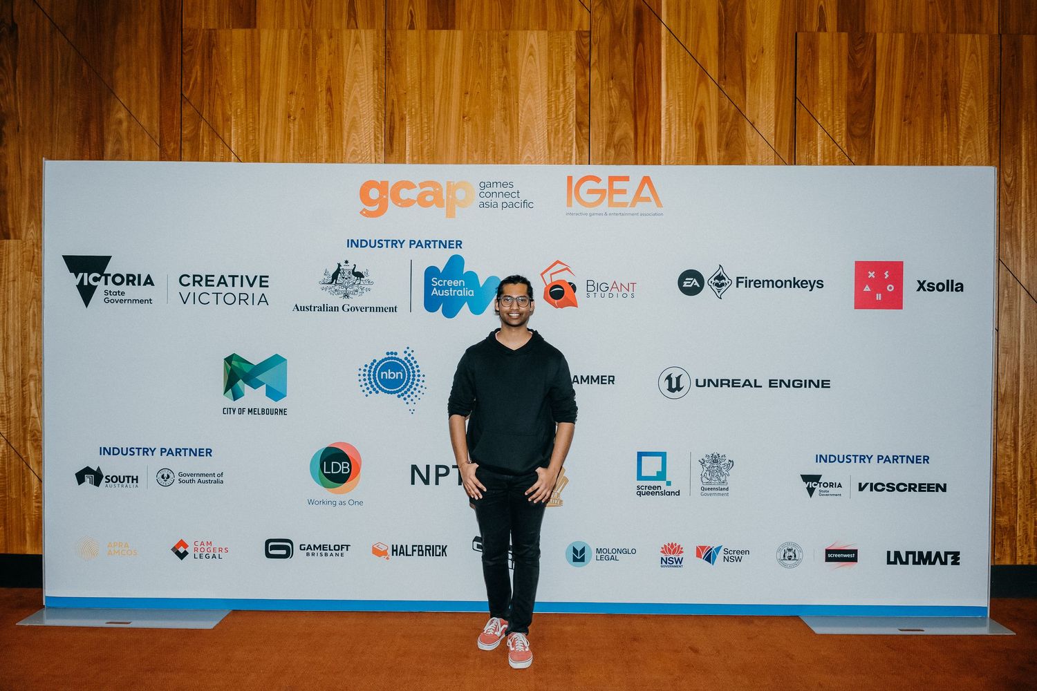 A long horizontal banner display with multiple corporate logos and sponsor branding against a wooden wall background.