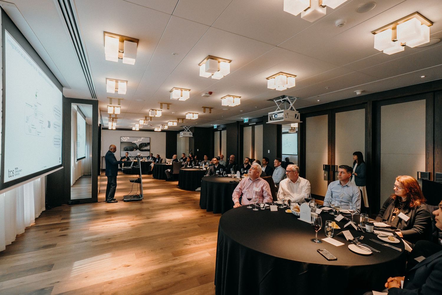 Modern office conference room with ceiling lights and projector screen during a business meeting.