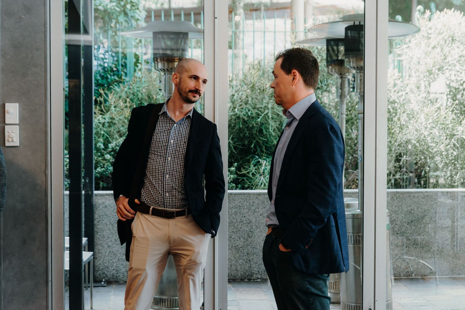 Two people in business attire having an animated conversation in a bright office hallway.