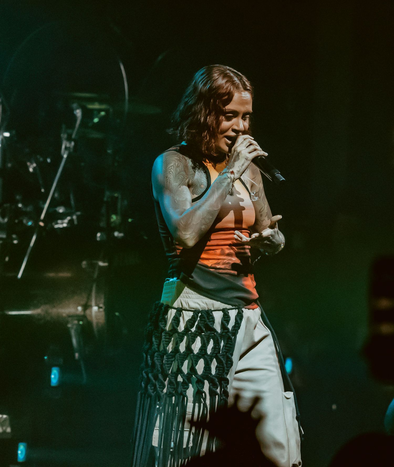 Singer performs emotionally on stage in a black and white striped skirt and orange top during a concert performance.