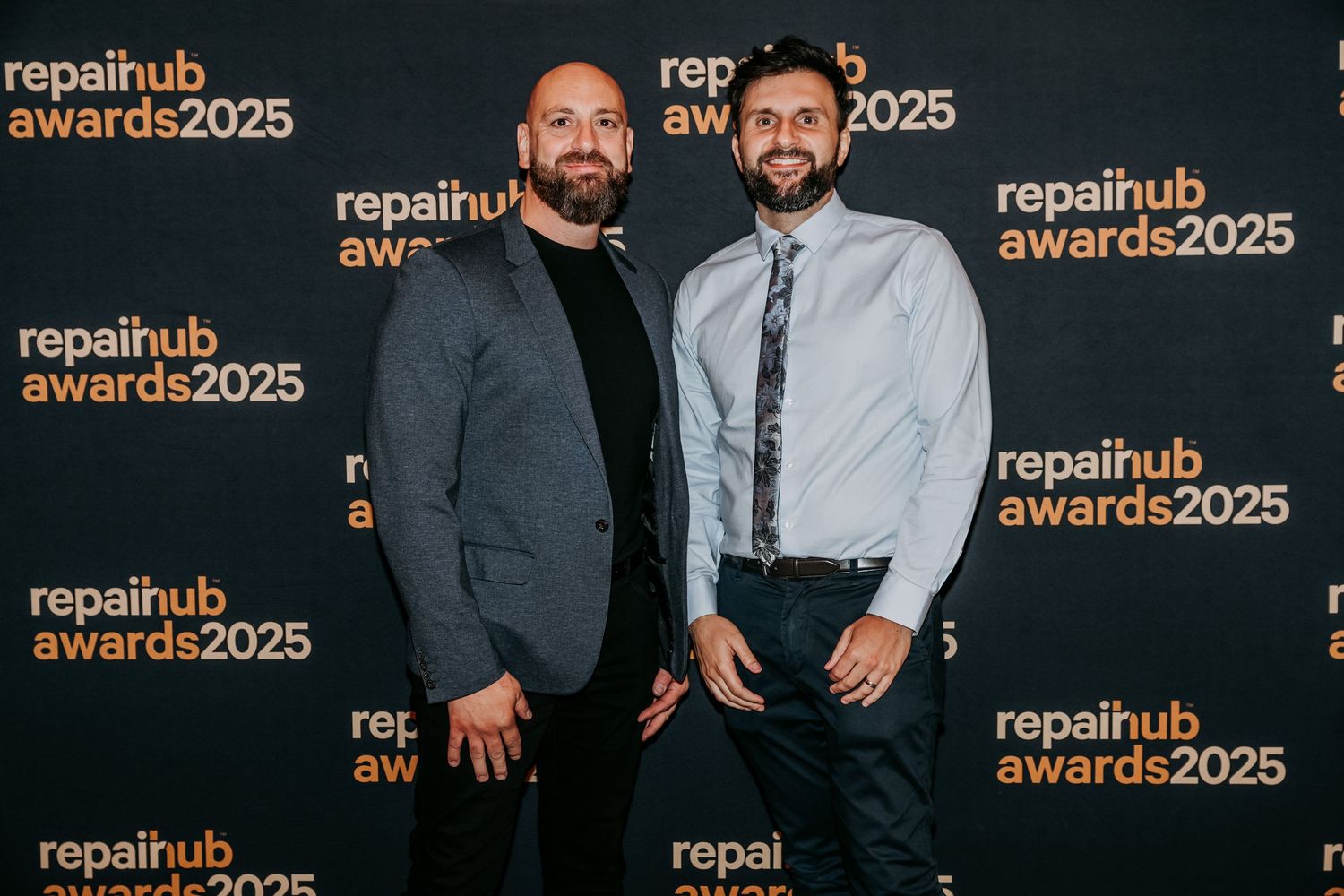 Two people in formal attire pose together at the RepaiHub Awards 2025 event against a branded backdrop.