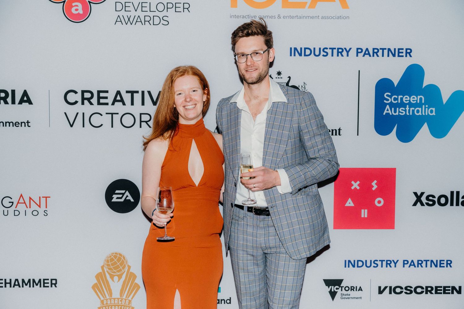 People in formal attire stand in front of a sponsor wall displaying tech company logos at an awards ceremony.