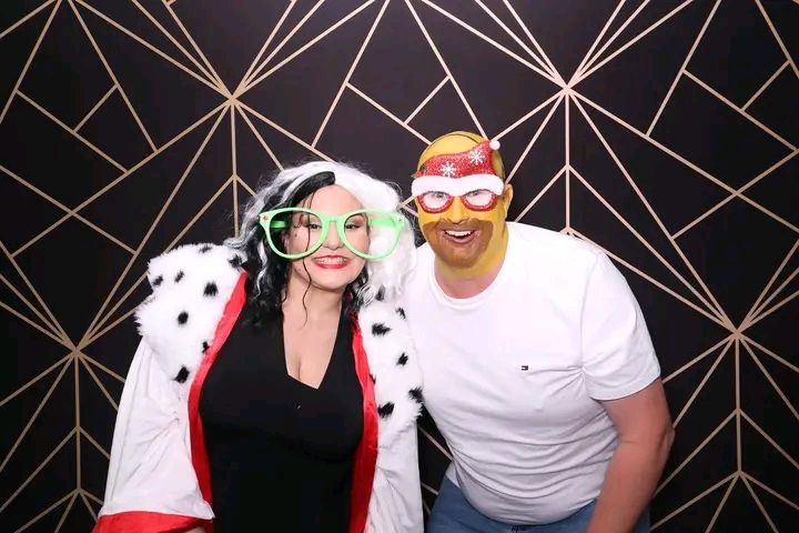 People posing together in a photo booth with fun props and accessories against a dark geometric patterned background.
