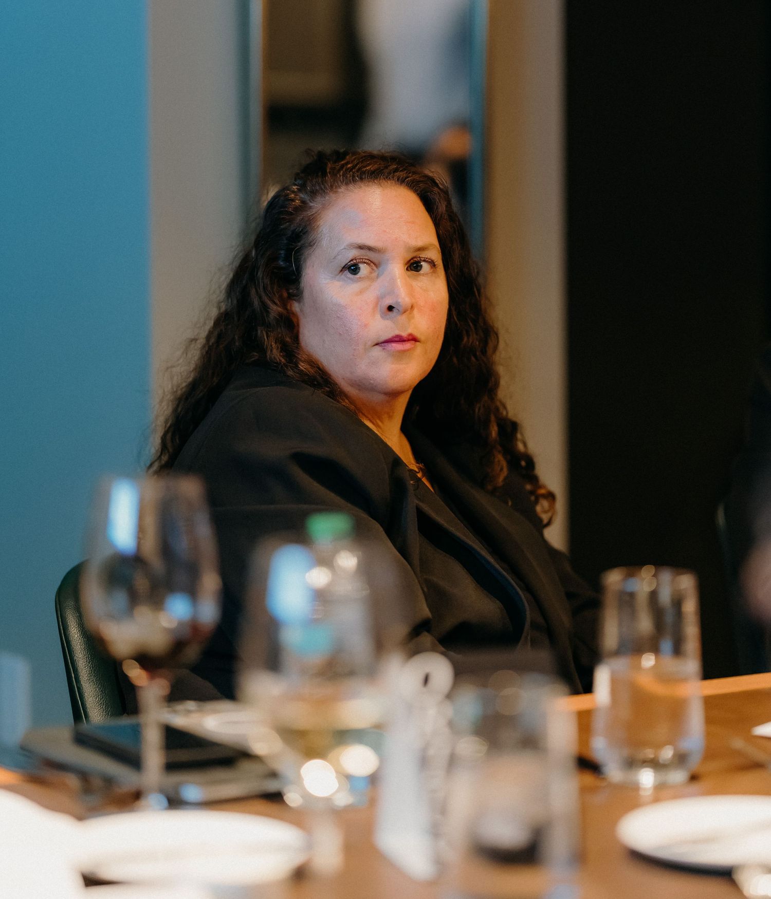 A person sits at a dimly lit table with glasses and dinnerware, creating a moody dining atmosphere.