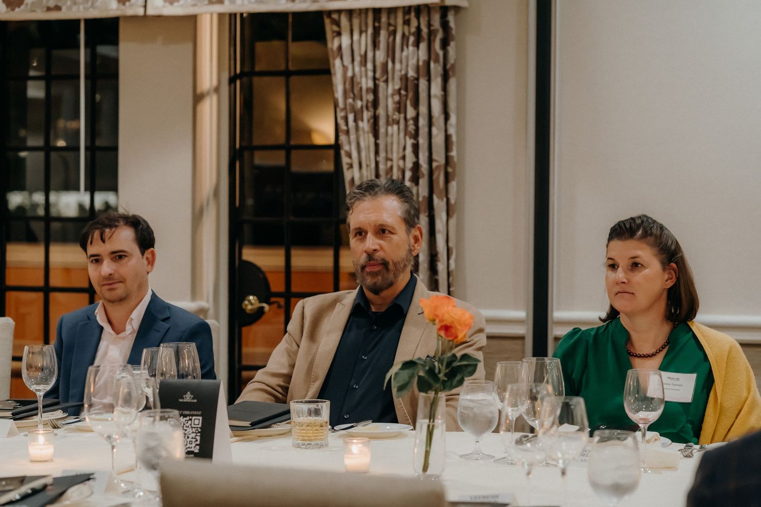 Business professionals gather around an elegant dining table with candlelight and wine glasses for a formal dinner meeting.