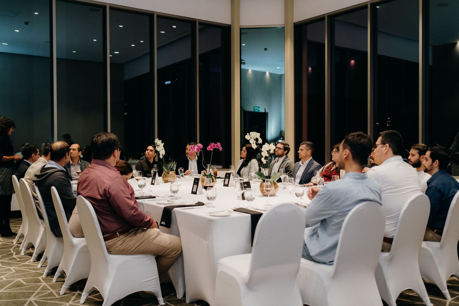 Elegant wedding reception setup with white-covered chairs and tables in a modern venue with large windows.