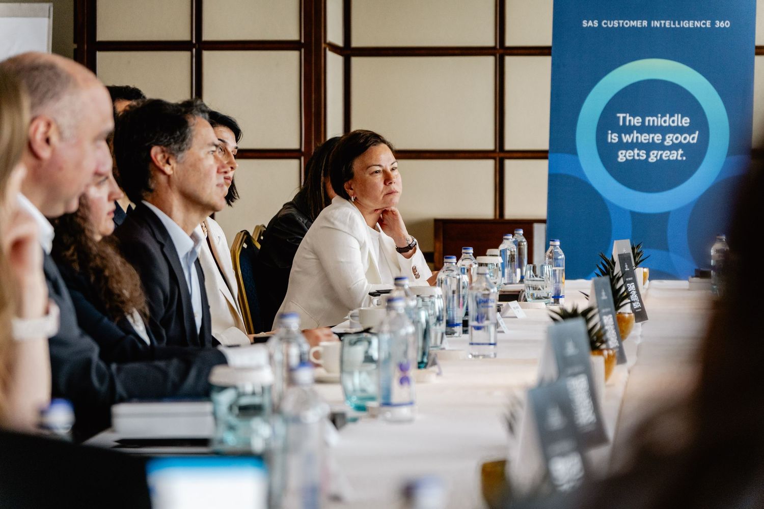 Business professionals seated at a conference table during a corporate meeting with a motivational banner in the background.