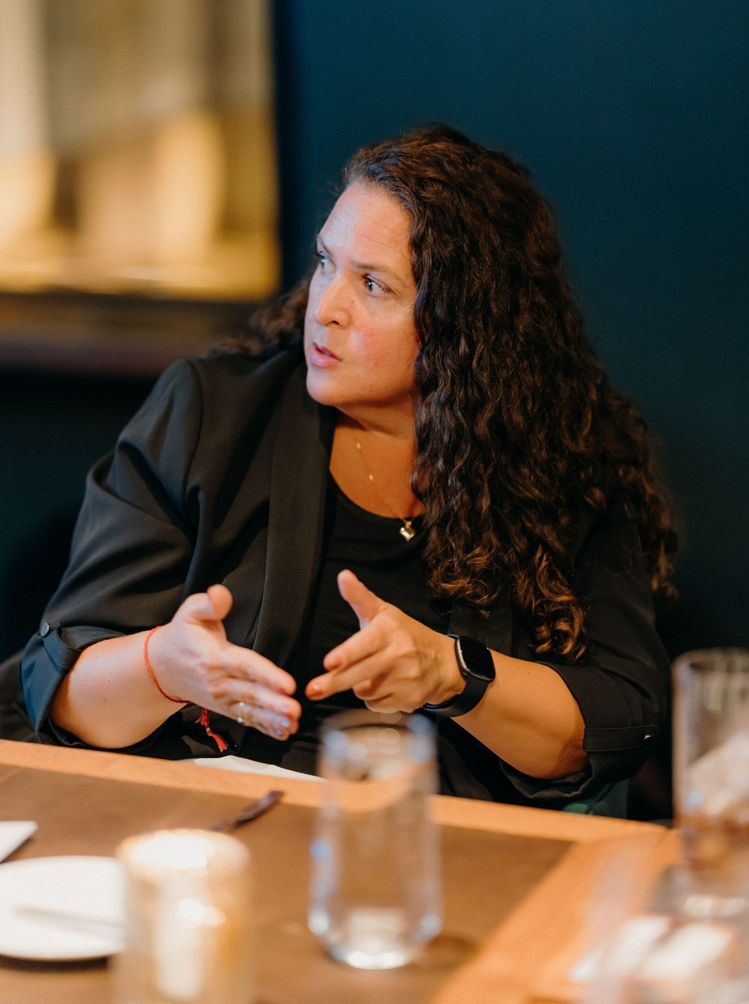 A person in a black shirt leans on a table in warm lighting, shown in a series of candid poses during conversation.