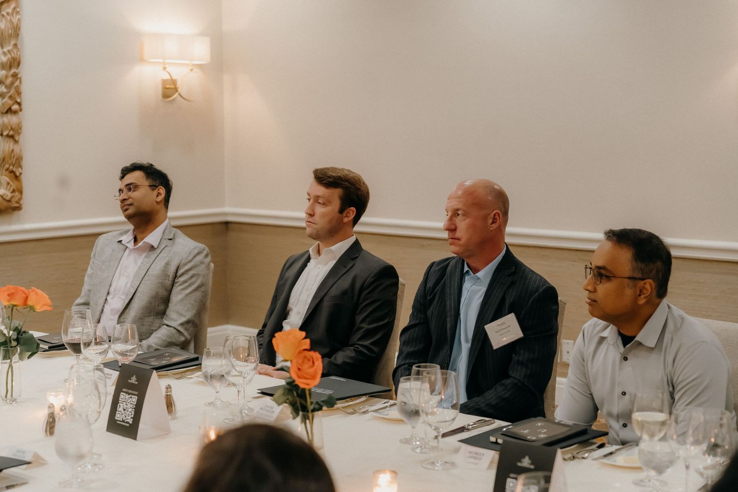 Business professionals seated at a conference table during a meeting with table settings and white walls.