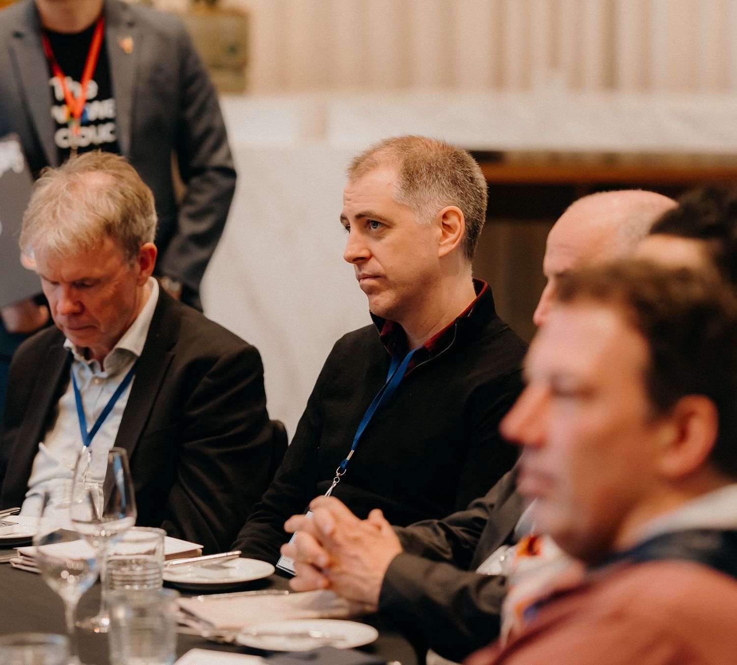 Business professionals seated at a conference table during a corporate meeting with water glasses and notepads.