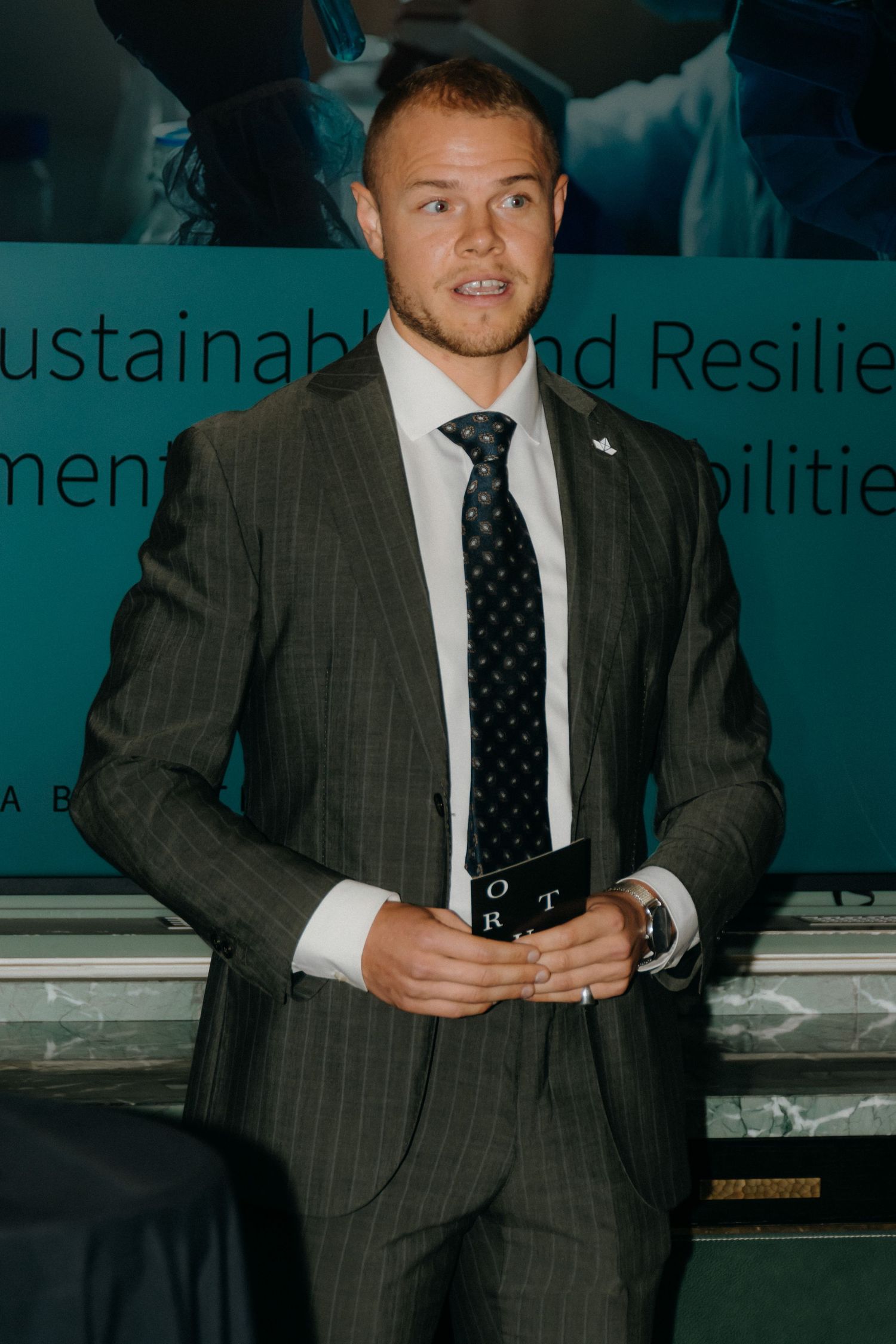 A person in a pinstriped suit and dark tie stands in front of a presentation display at a professional event.