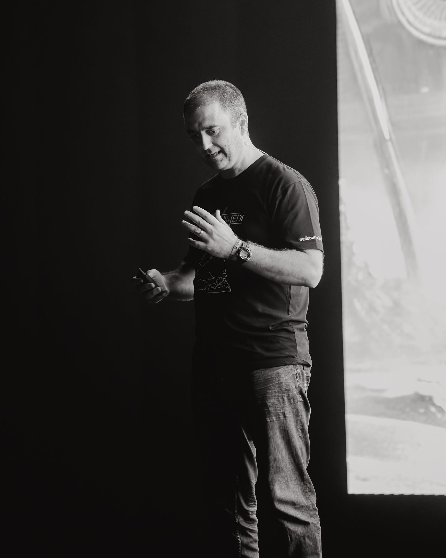 A series of black and white photos showing a person in a dark t-shirt gesturing while presenting against a dark background.