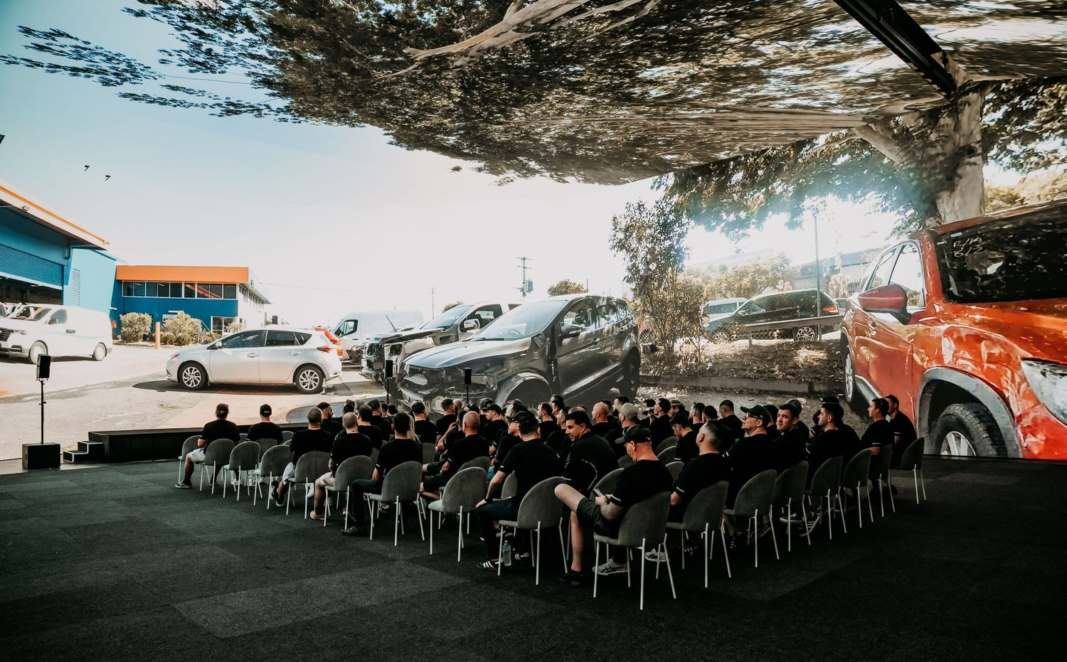 A large audience seated in rows of chairs under a vintage aircraft display at an aviation museum event.