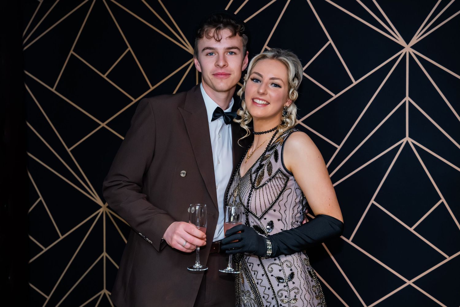 Couples in formal attire pose and celebrate at an elegant black and gold themed party.