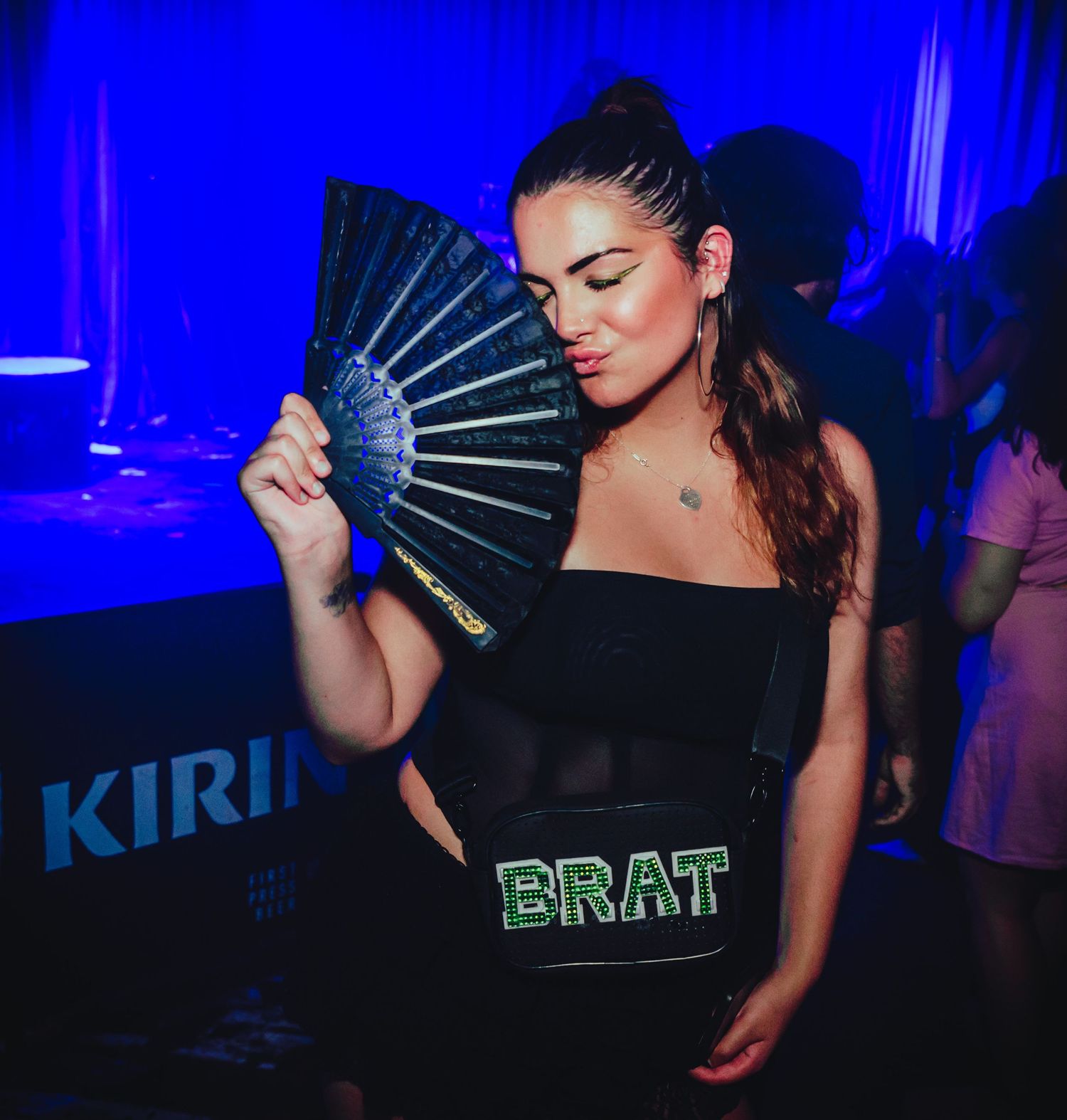 A figure in blue lighting holds a decorative fan while posing in an atmospheric nightclub setting.