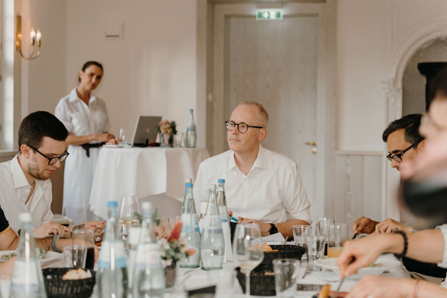 Business professionals seated at a dining table during a corporate meeting in an elegant white conference room.
