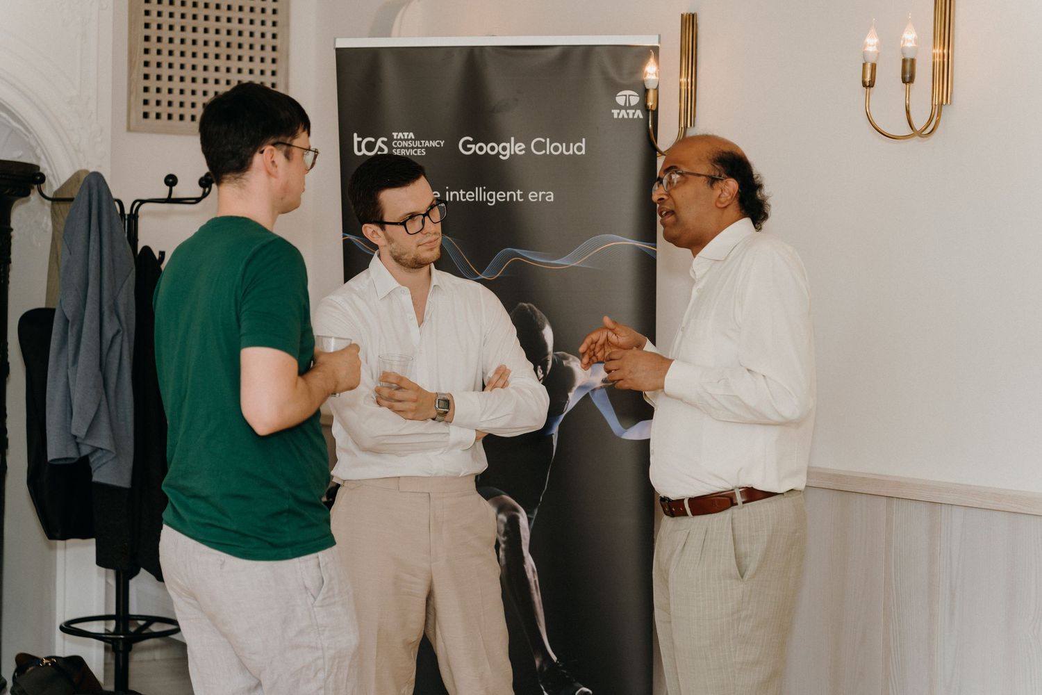 Three professionals networking at a TCS and Google Cloud event, engaged in conversation near a branded banner.