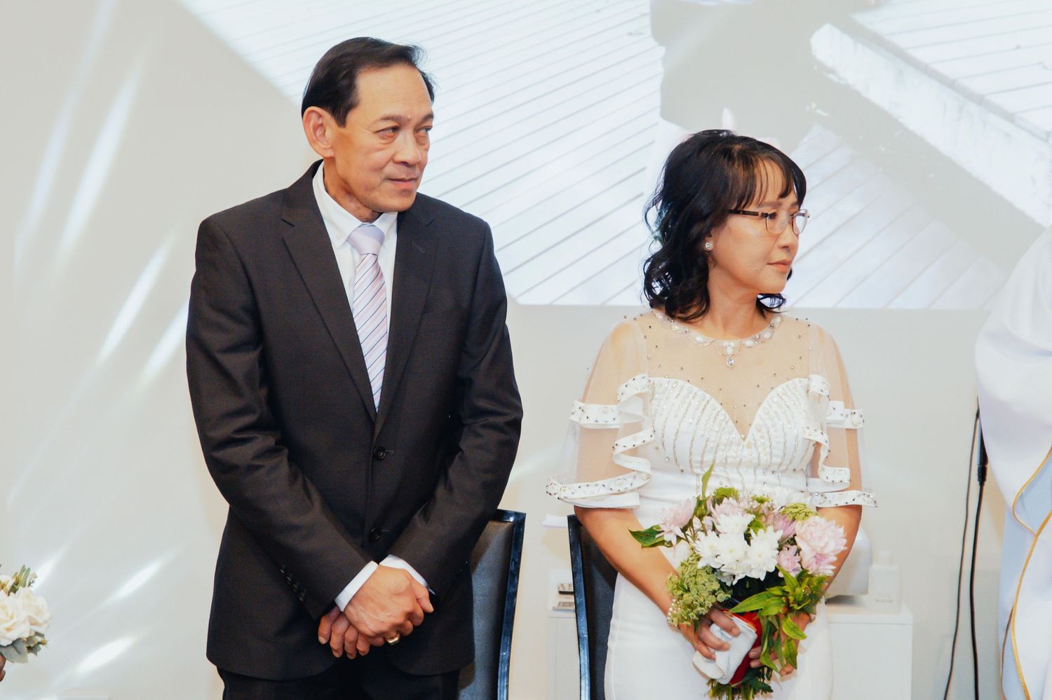 Couple in formal wedding attire during ceremony with bride wearing white dress and groom in dark suit.