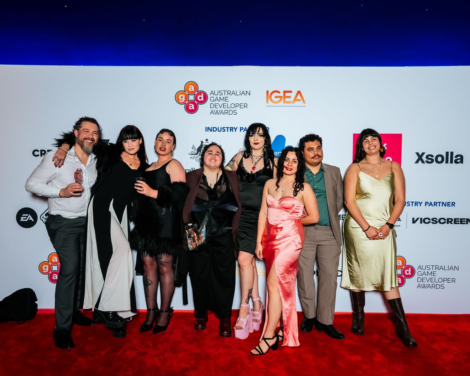 A group poses together on a red carpet event with a branded backdrop featuring corporate sponsor logos.
