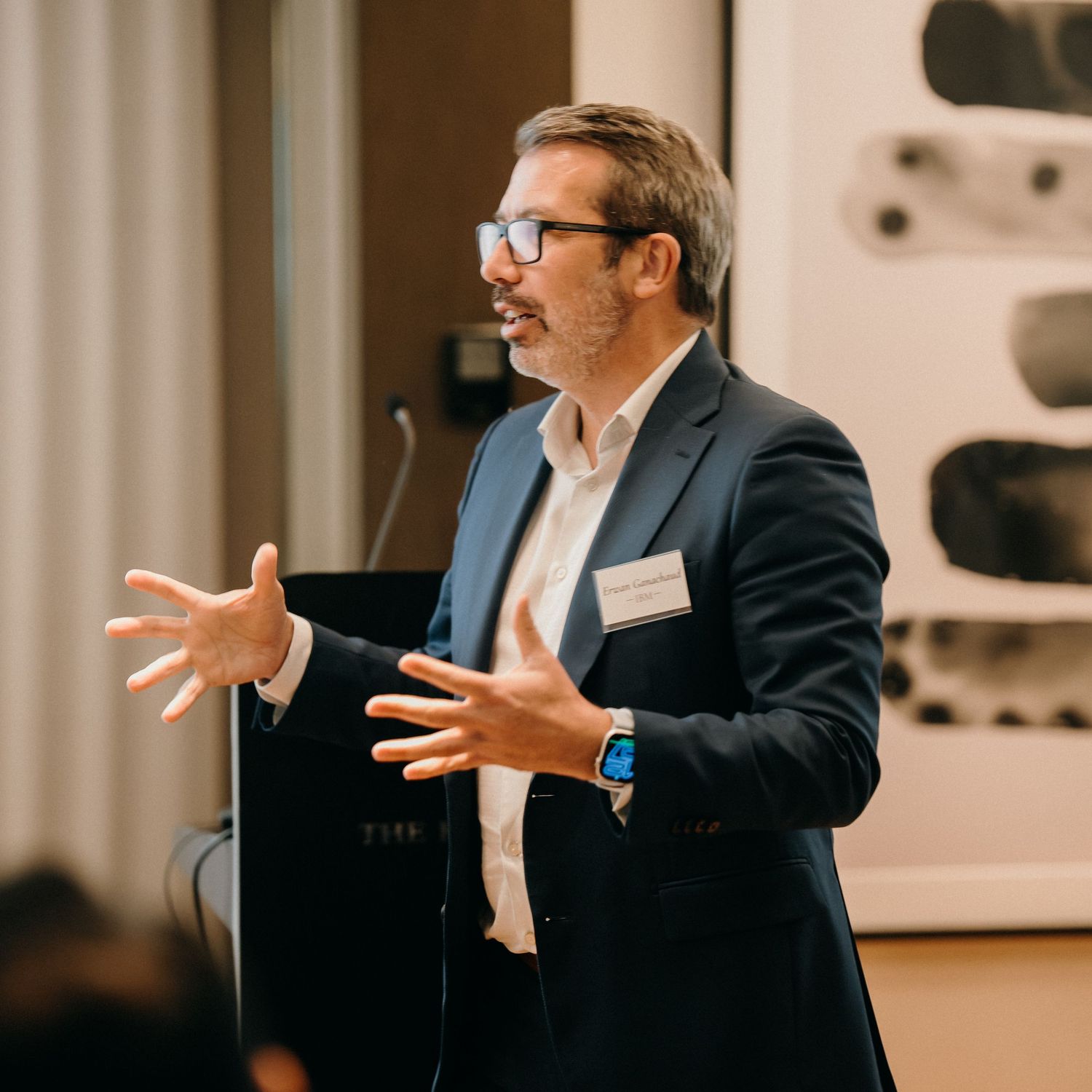 Professional speaker wearing a suit gestures enthusiastically while presenting during a business meeting.
