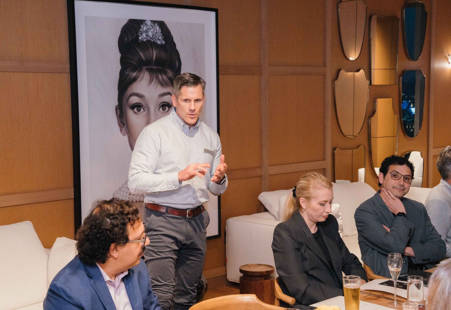 People seated at tables in a business conference room during a meeting or presentation.