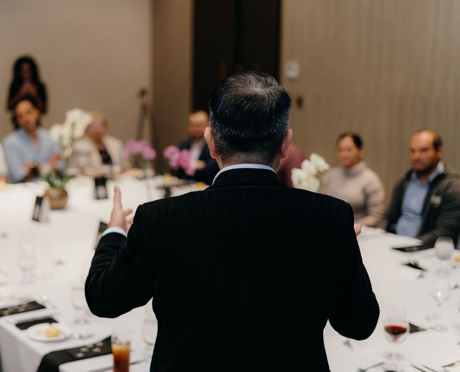 Business professionals sit at round tables during a formal dinner event in an elegant conference room setting.