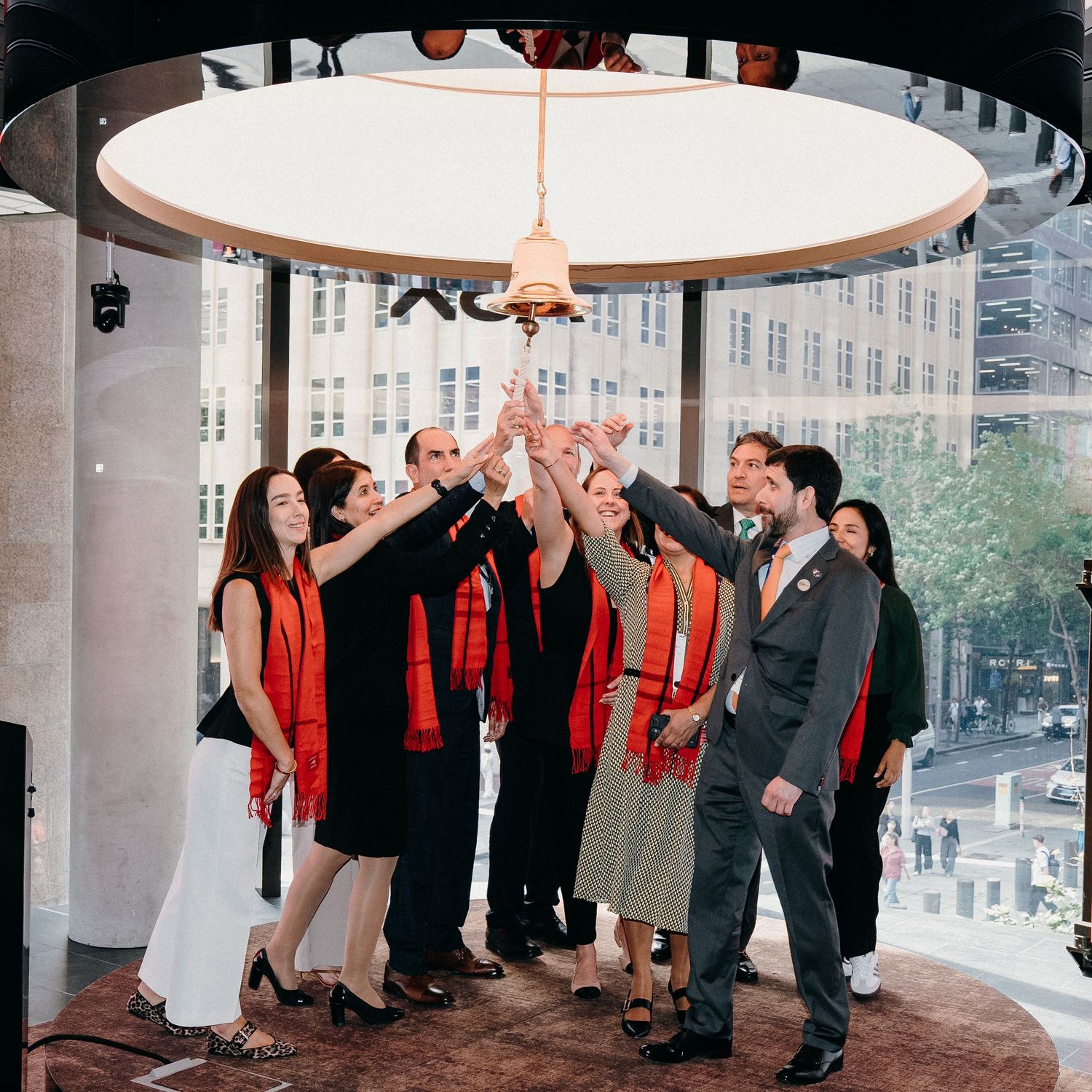 Group of people in red and black attire dancing and celebrating in a circular formation under a white ceiling light.