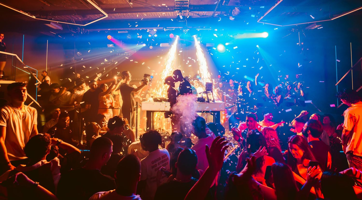 A vibrant nightclub scene with colorful blue and red lighting illuminating a crowded dance floor during a party.