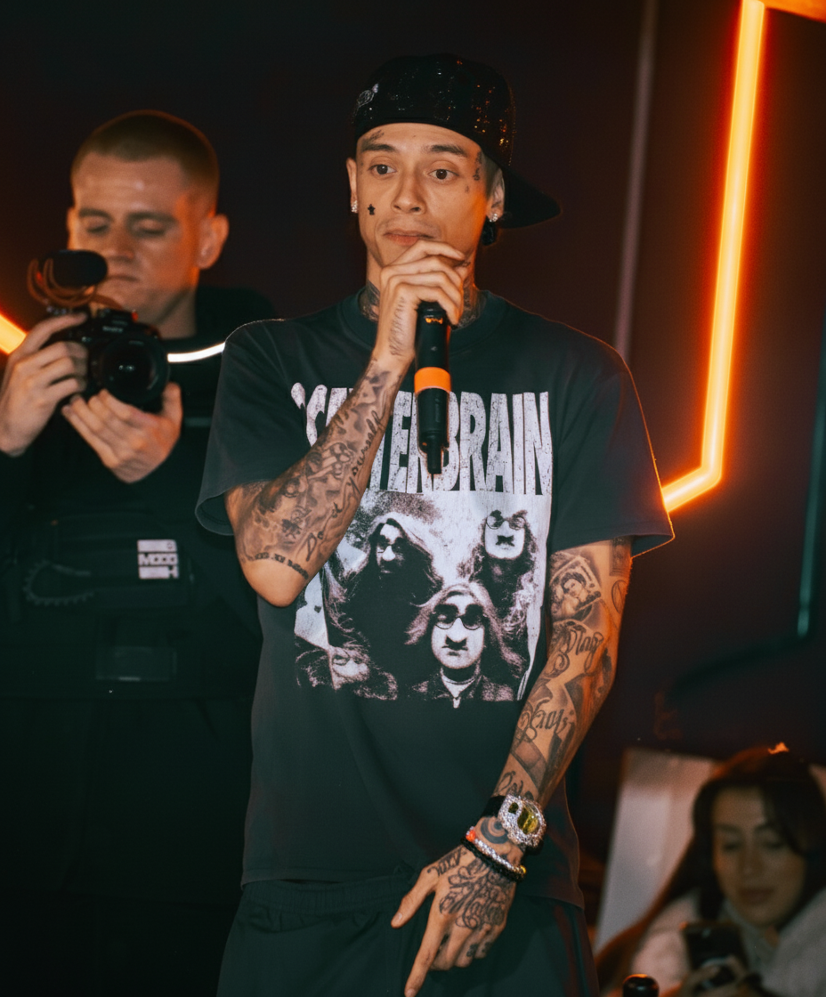 A person with tattoos performs on stage with orange lighting effects in the background.