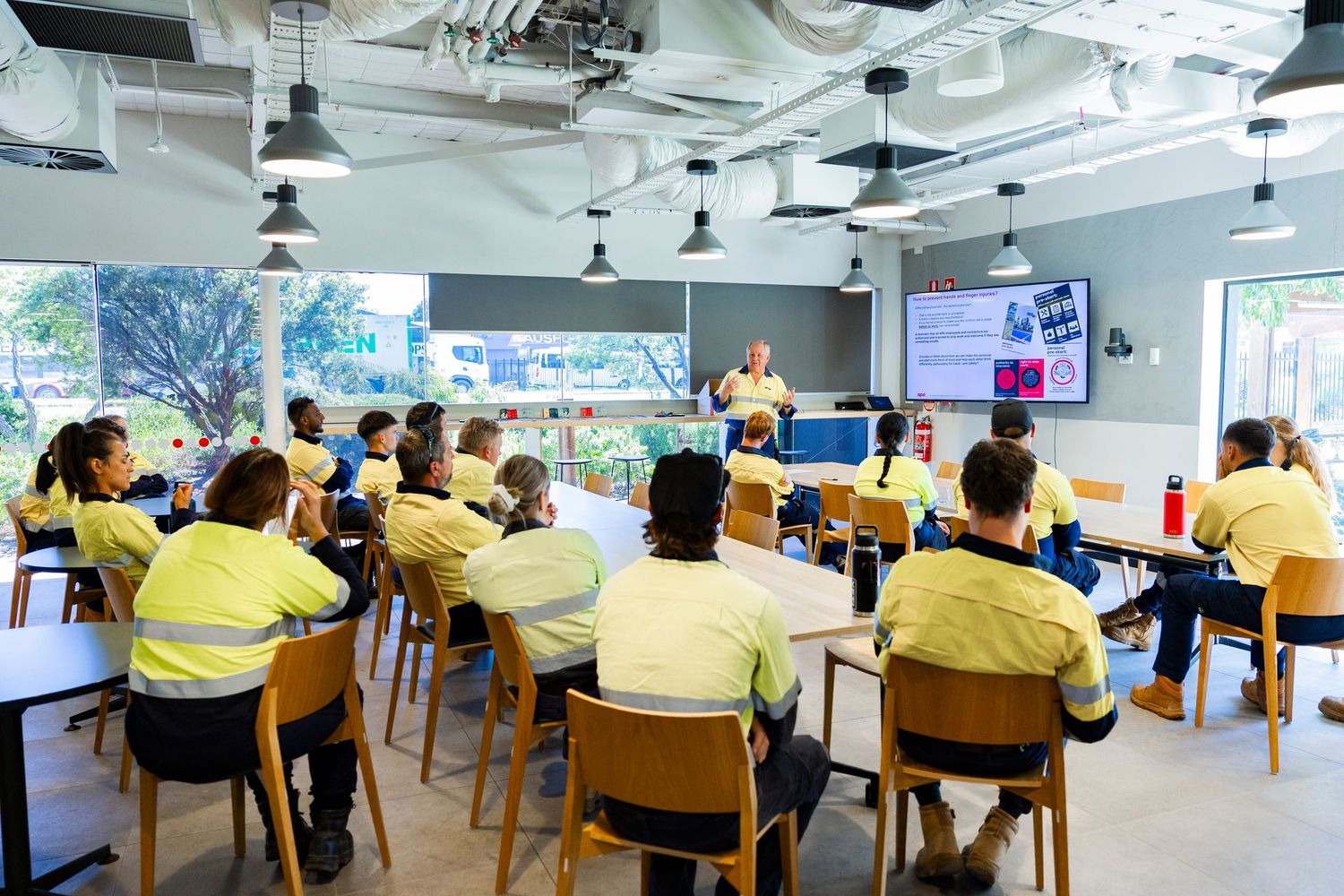 Students seated in rows attend a classroom training session with presentation screens visible at the front.