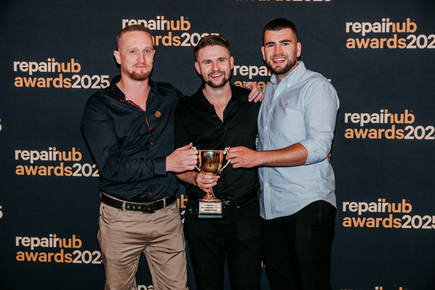 People in black attire posing together at an awards ceremony with Repairhub branding banners in the background.