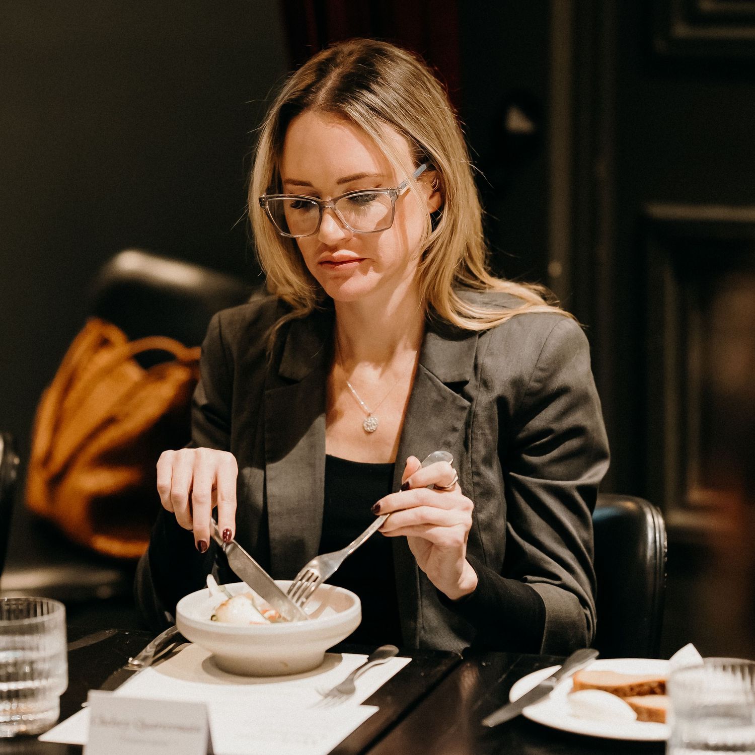 Professional woman in business attire dining at an upscale restaurant while working on a laptop.
