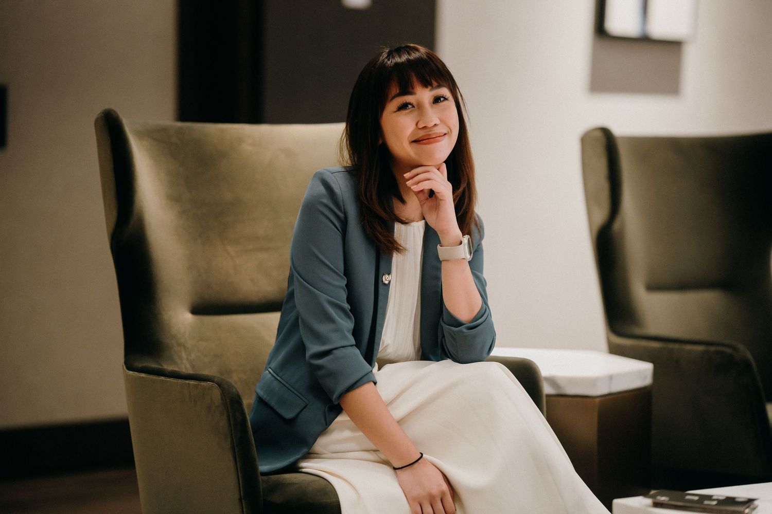 Woman in blue blazer sits thoughtfully in modern office chair while working at desk.