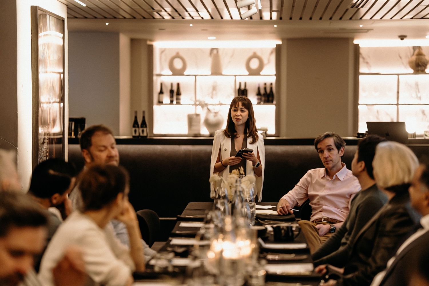 Diners seated at a modern restaurant bar with warm lighting and wooden slat ceiling details.