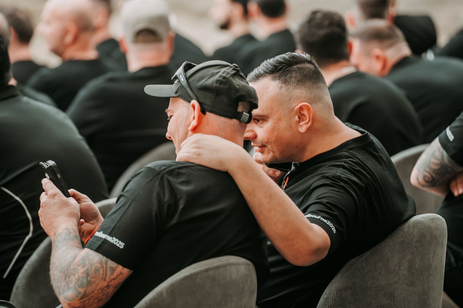 A row of people wearing black clothing sit together in a dark room during an event.