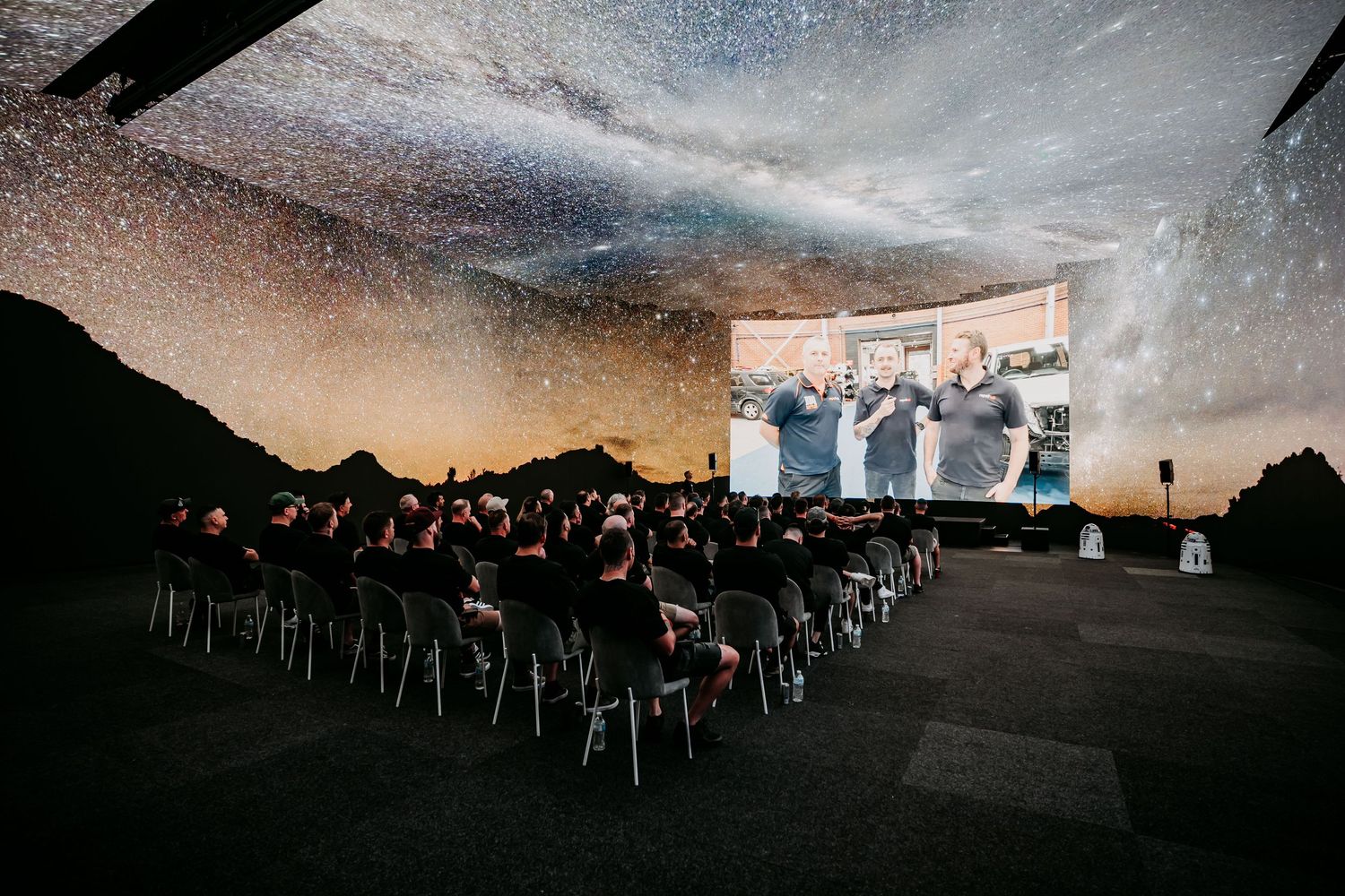 A group of stargazers gather at night under a starlit sky with telescopes and chairs set up for astronomical viewing.