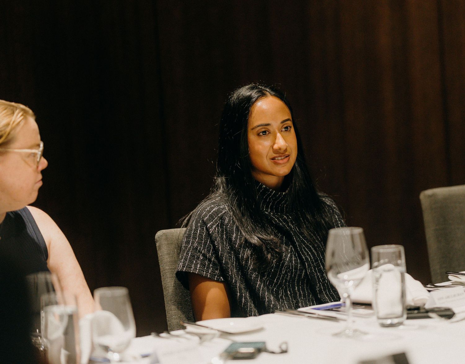 Two women seated at a formal dining table during a professional event, engaged in conversation.