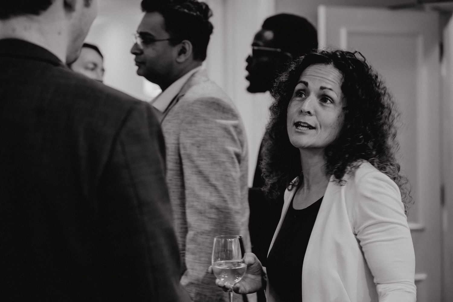 A black and white photo collage shows people in formal attire mingling at an indoor social gathering.