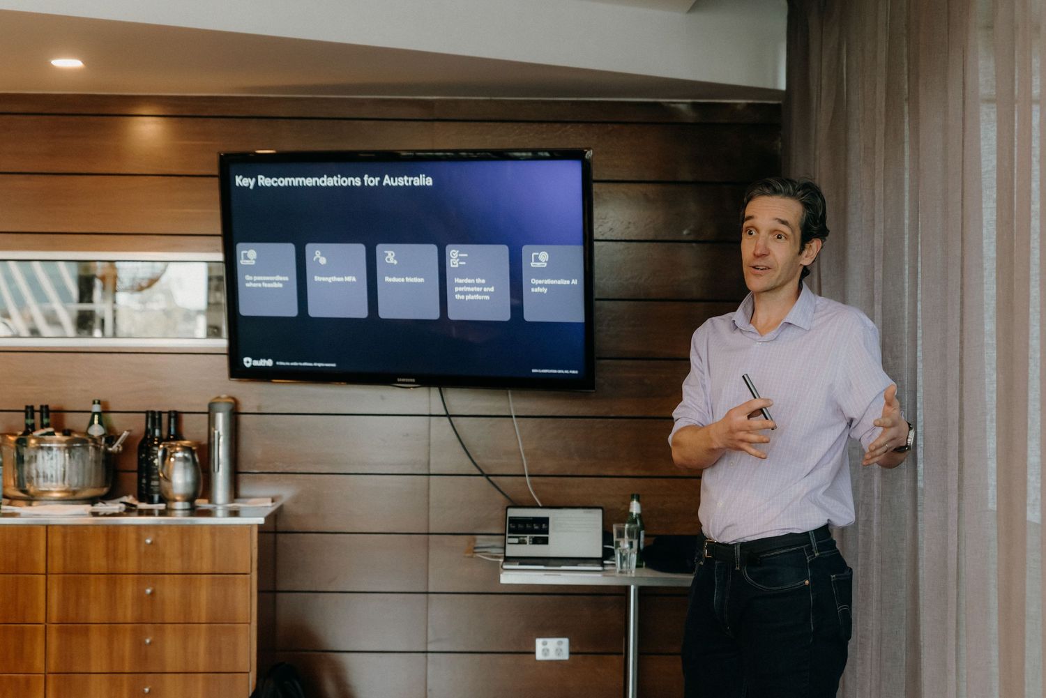 Professional presenter giving a business presentation in front of a wall-mounted TV display in a modern office setting.