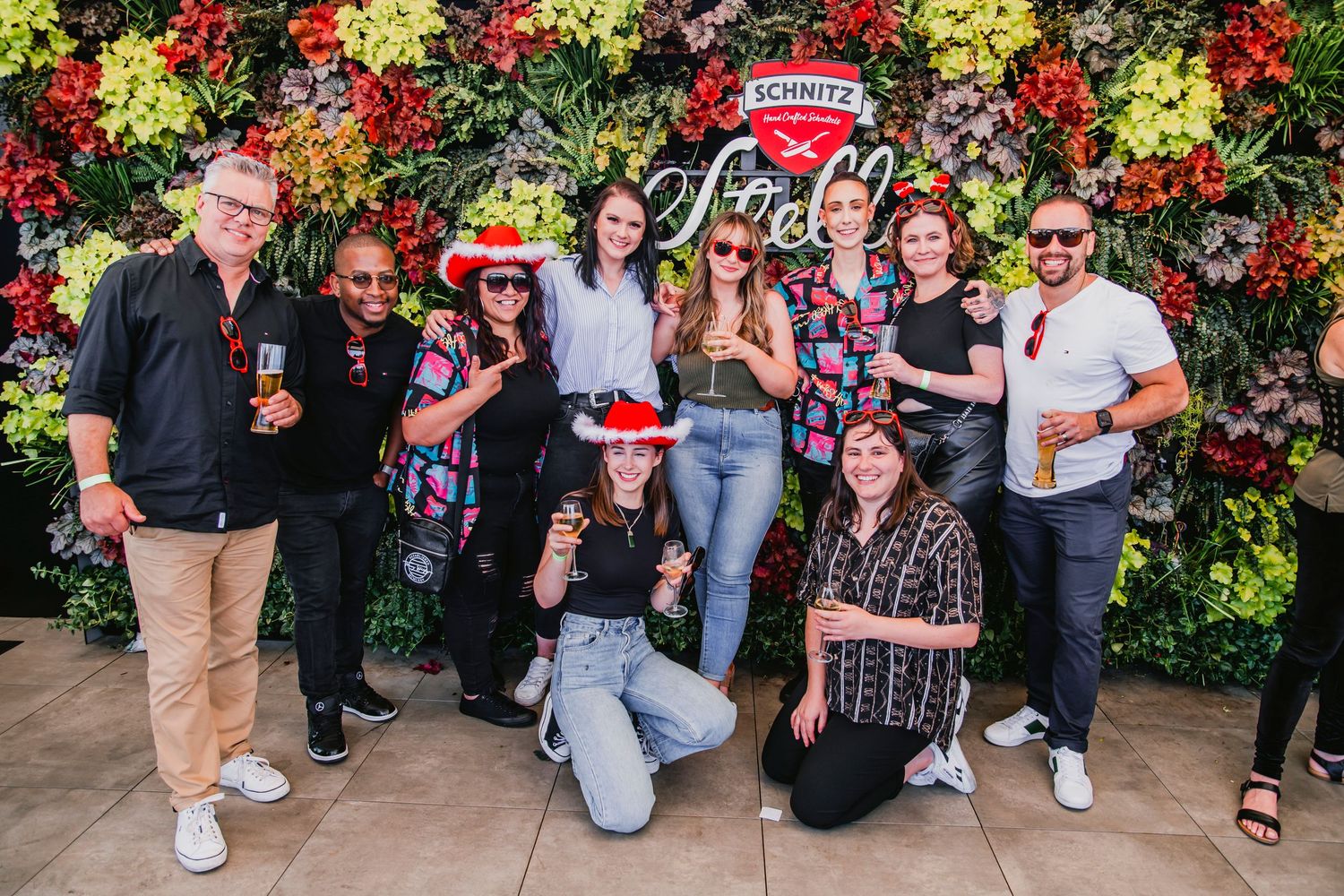A group poses together at a festive event with a colorful floral wall and Stella Artois branding in the background.