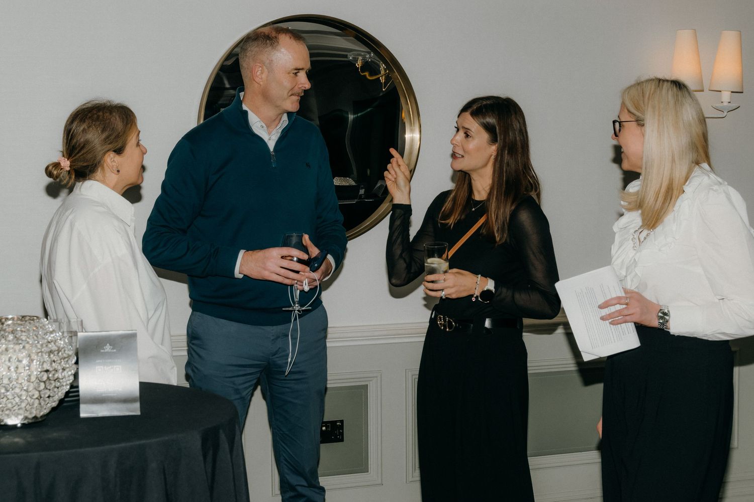 People in business attire engage in casual conversation during a networking event in a bright office space.